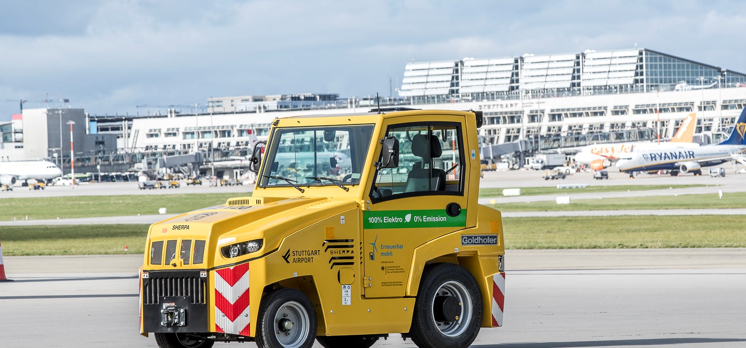 Ein elektrisch betriebener Cargo-Schlepper steht auf dem südlichen Stuttgarter Flughafenvorfeld. Im Hintergrund stehen die Terminalgebäude. 